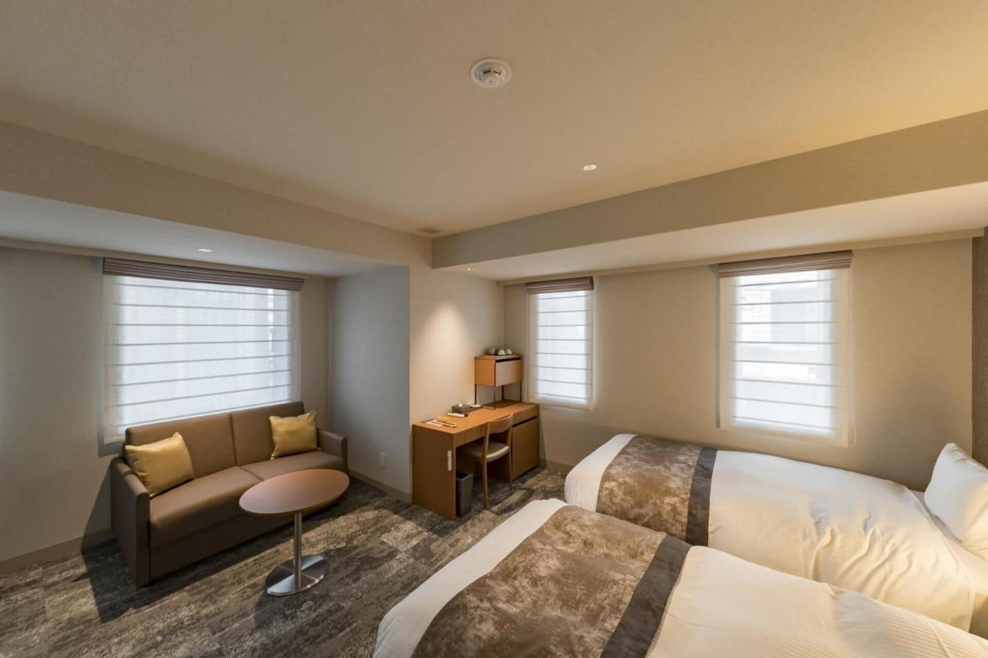 A hotel room with a sofa, a desk, and two beds.