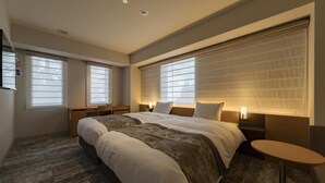 Una habitación de hotel moderna con una cama grande, dos mesitas de noche, un escritorio y una pequeña mesa redonda.