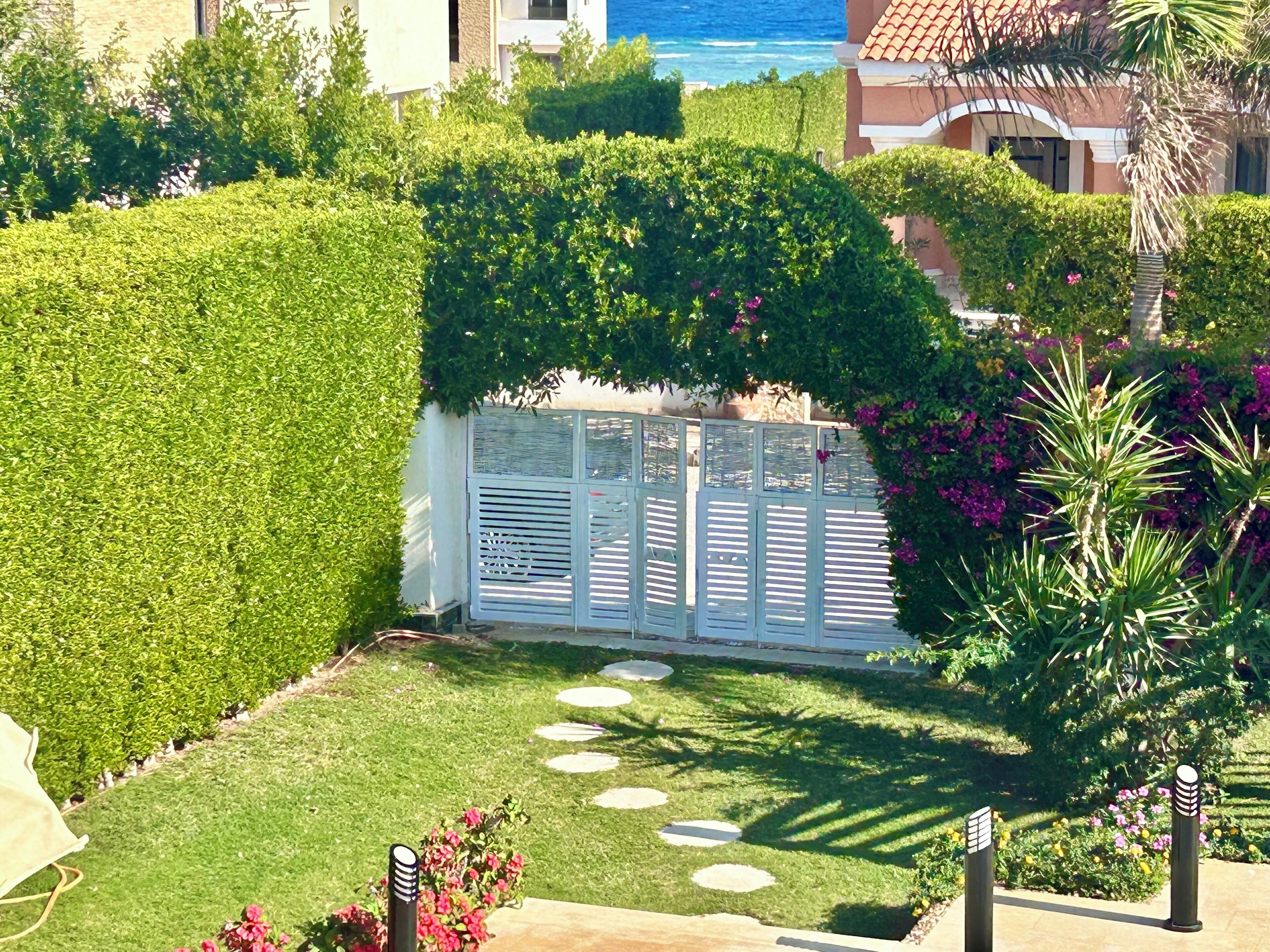 Ein gepflegter Garten mit einer Hecke, einem weißen Tor und einem Weg, der zu einem Gebäude führt.