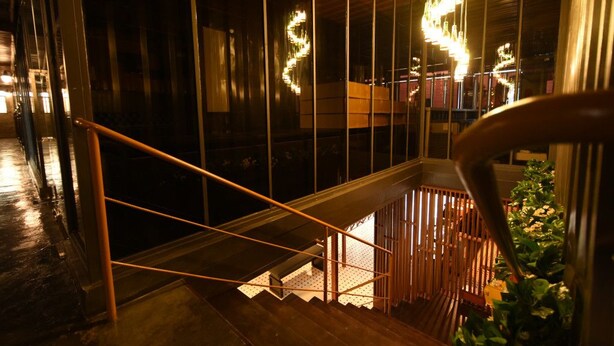 A staircase with a wooden handrail, metal balusters, and a glass balustrade reflecting interior lights. - Hotel Snow Angeles (Angeles City)