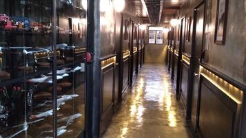A corridor with a polished floor reflecting lights, glass display cases on the left, and doors on the right.