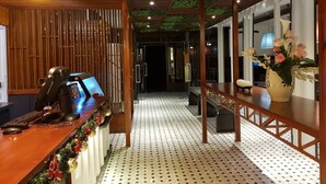 A reception area with a wooden desk, a computer, and a telephone. There is a decorative garland on the desk and a plant on the right side. - Hotel Snow Angeles (Angeles City)