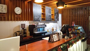 A coffee shop interior with a wooden ceiling, a coffee machine, a menu board, and a clock indicating 7:30. - Hotel Snow Angeles (Angeles City)