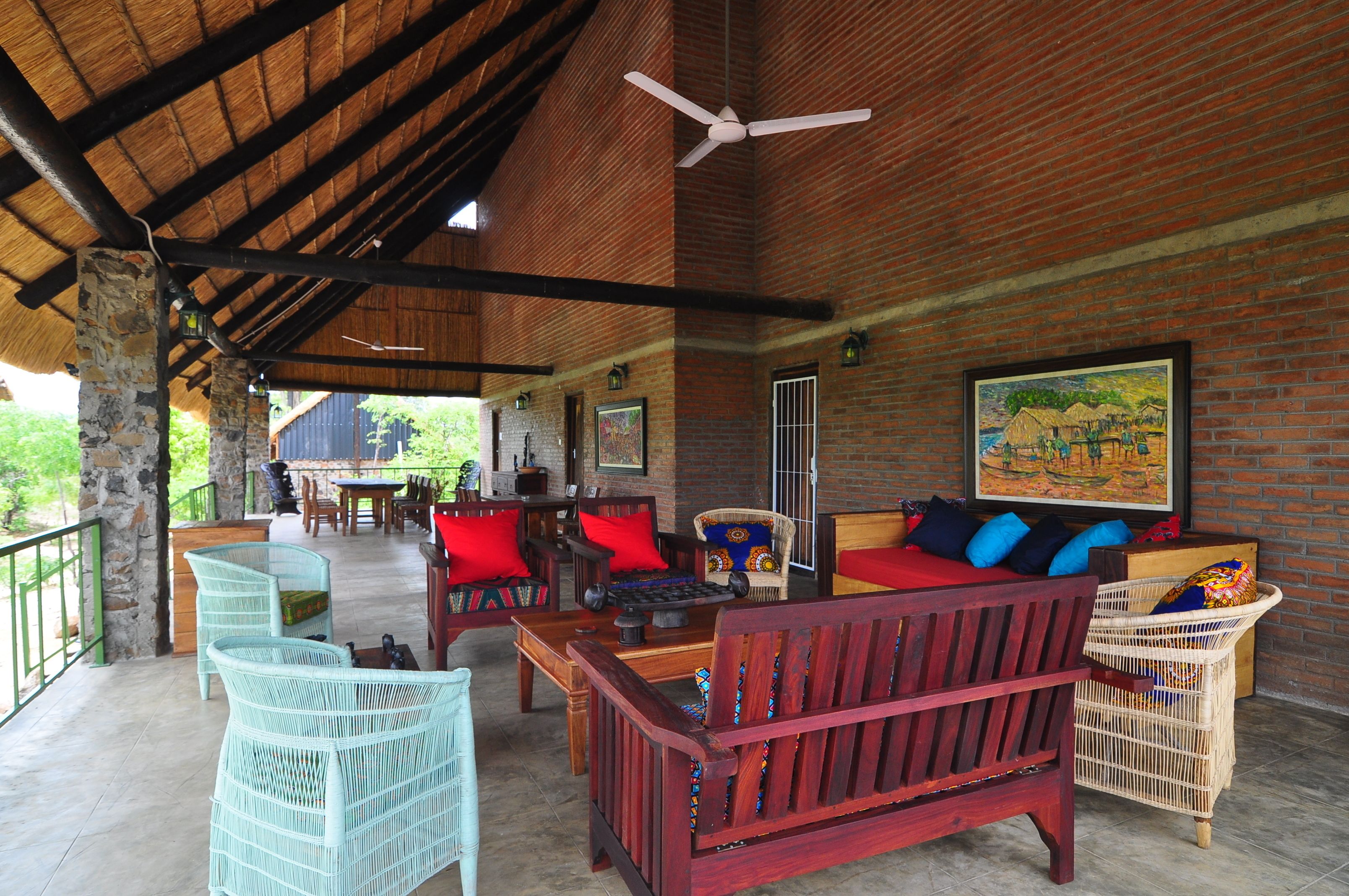 A spacious outdoor seating area with wicker furniture and a red sofa, a ceiling fan, and a brick wall with a painting.