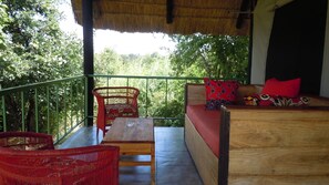 A wooden bench, a red wicker chair, and a sofa with red cushions on a balcony with a green railing.