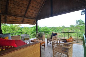 A covered outdoor seating area with wicker furniture and a view of lush greenery.