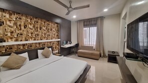 Quarto de hotel com cama, escrivaninha, cadeira, televisão e ventoinha no teto.