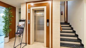 An elevator with a digital display, a staircase with black steps, and a plant in a white pot.