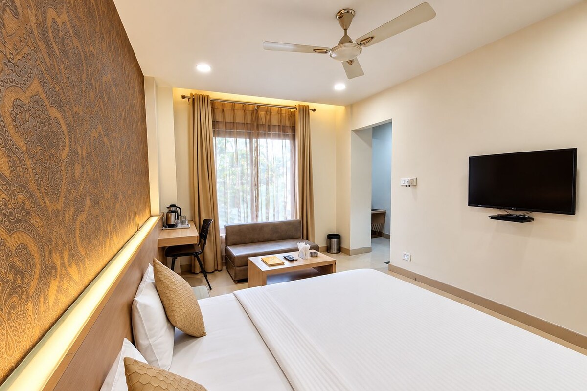 A hotel room with a bed, a desk, a sofa, a television, and a ceiling fan.