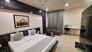 Habitación de hotel con cama, escritorio, silla, televisor y un cuadro en la pared.