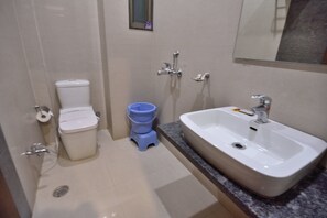 Casa de banho com sanita, bidé, lavatório e um balde azul.