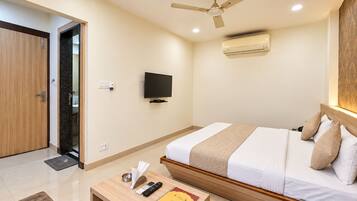 A hotel room with a bed, a television, a ceiling fan, and an air conditioning unit.