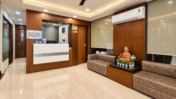 A reception area with a reception desk, a ceiling fan, a wall-mounted air conditioner, and a Buddha statue on a table.