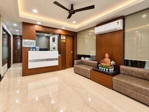 A reception area with a reception desk, a ceiling fan, a wall-mounted air conditioner, and a Buddha statue on a table. - Hotel Alankar Palace (Bhopal)