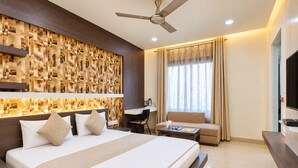A modern hotel room with a large bed, a desk, a sofa, a television, and a ceiling fan.