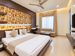 A modern hotel room with a large bed, a desk, a sofa, a television, and a ceiling fan. - Hotel Alankar Palace (Bhopal)