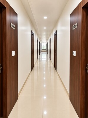 A hotel corridor with wooden doors, numbered 105 and 106, and a shiny tiled floor. - Hotel Alankar Palace (Bhopal)