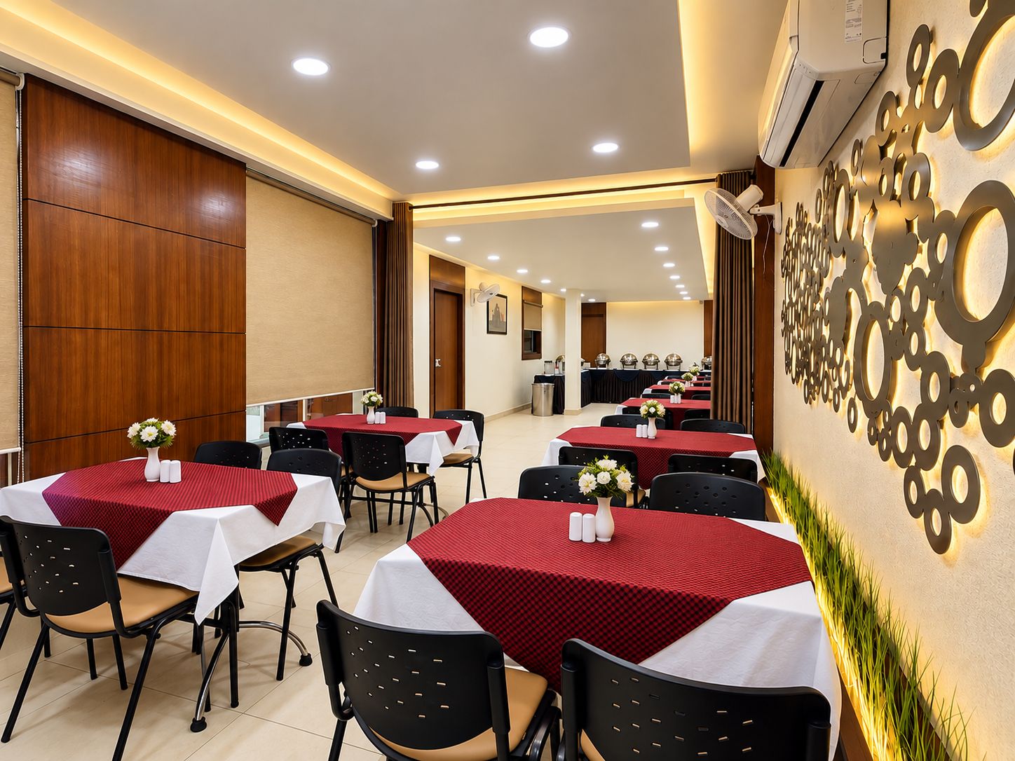 A hotel dining area with round tables, black chairs, and red tablecloths.