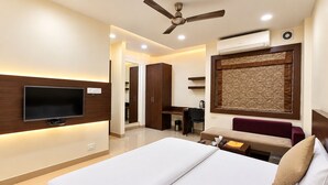 A hotel room with a bed, a television, a ceiling fan, and a desk with a chair.