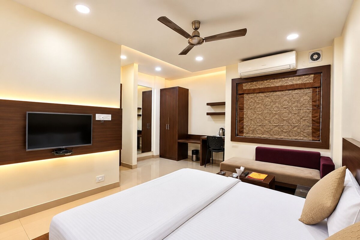 A hotel room with a bed, a television, a ceiling fan, and a desk with a chair.