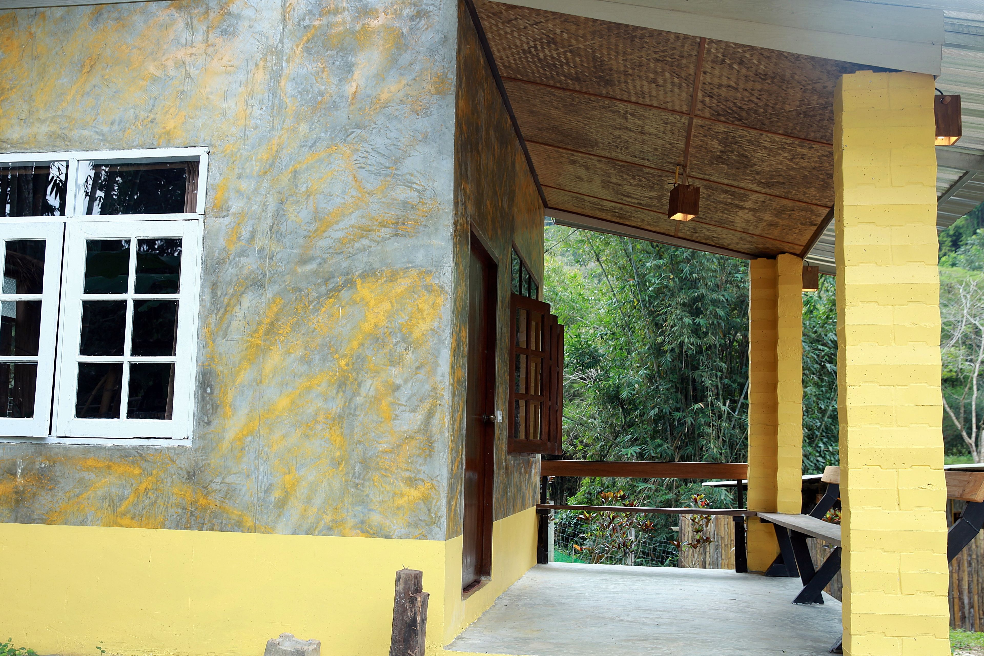 A covered outdoor area with a concrete floor, wooden benches, and a yellow wall.