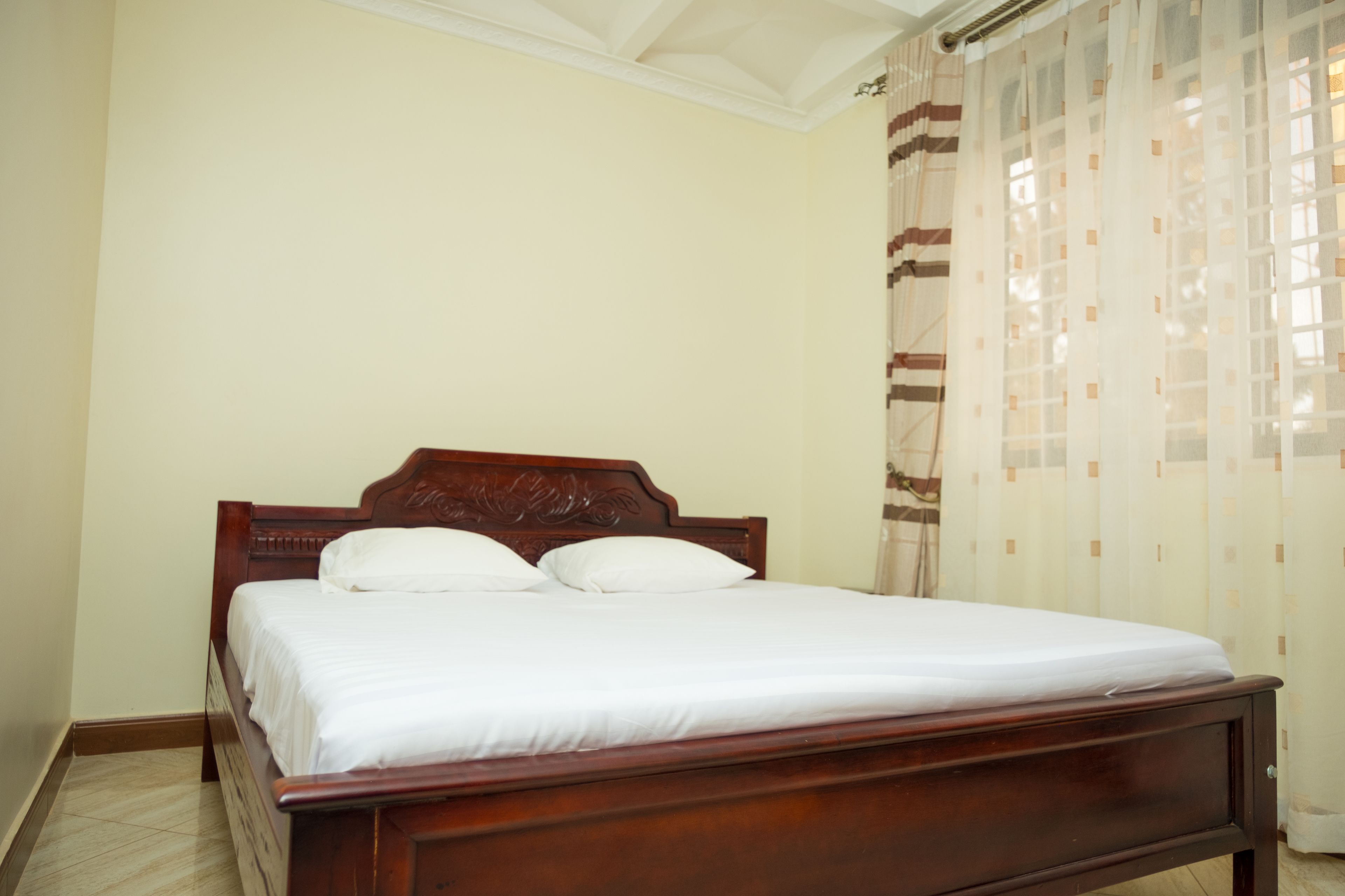 A single bed with a wooden headboard and white bedding in a room with cream walls and a patterned curtain.