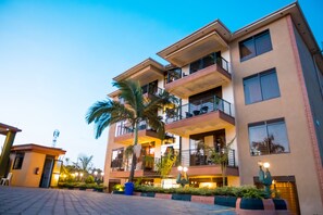 A multi-story hotel with balconies, palm trees, and a paved entrance area. - Kampala Suburbs Apartment (Kampala)
