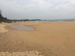 A wide sandy beach with a small puddle of water, palm trees, and a distant view of the ocean. - Jurys Bungalow (Hikkaduwa)