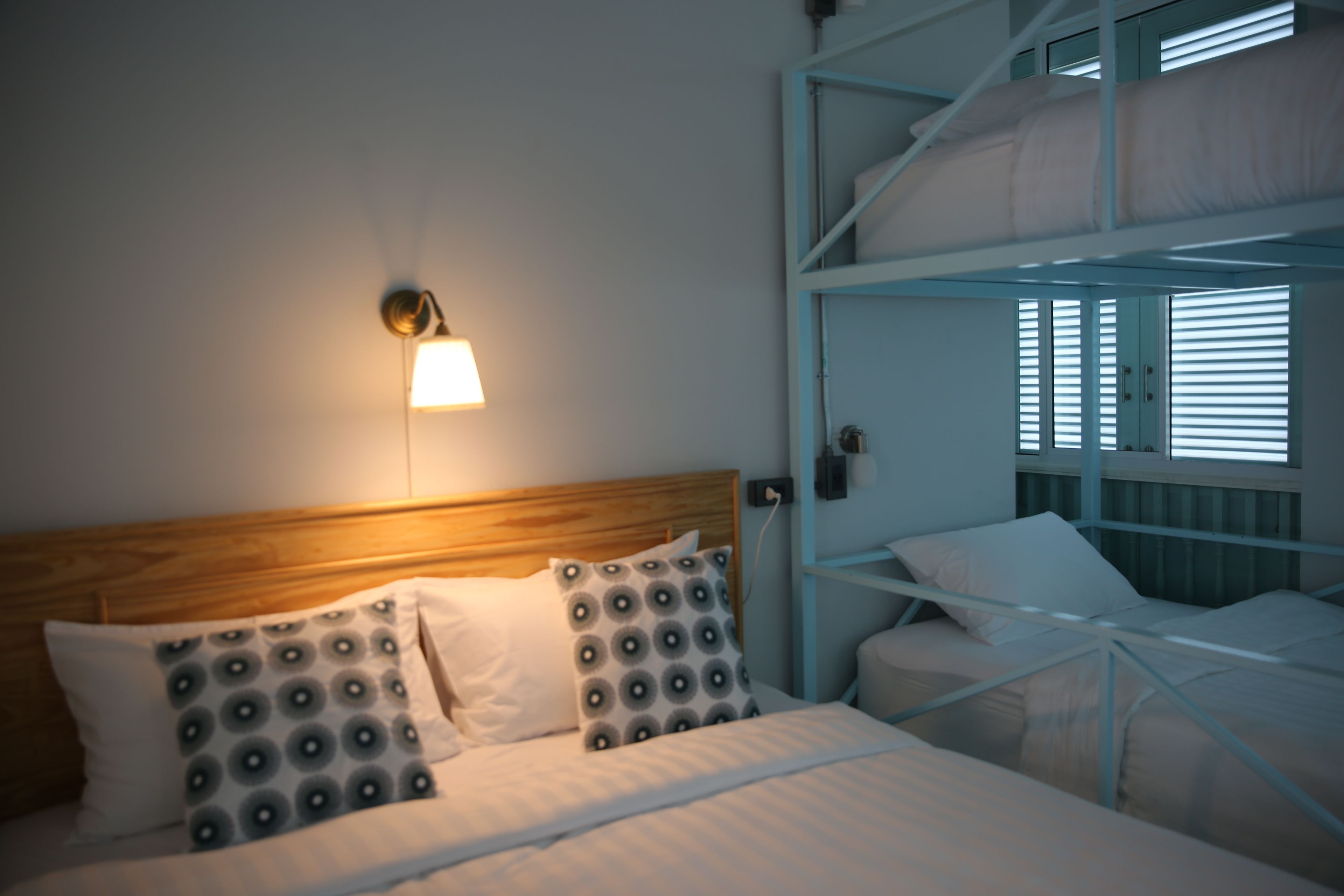 A bunk bed room with a wooden headboard, a wall-mounted lamp, and a window with blinds.