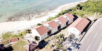 A coastal hotel with a row of white buildings with red roofs, situated by a sandy beach and the sea.