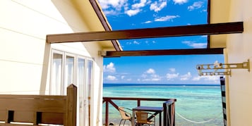 A balcony with a view of the ocean, a wooden chair, and a table.
