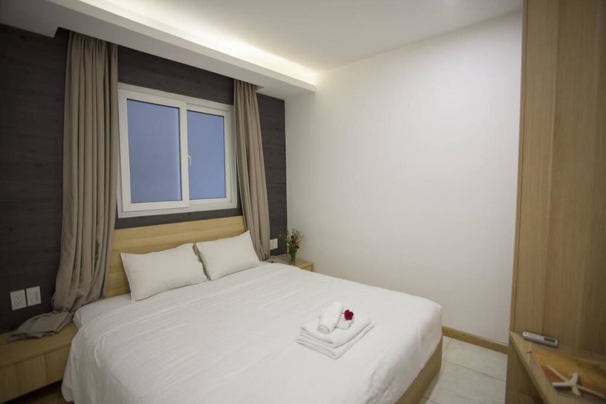A neatly made bed with white linens and a folded towel with a red rose.