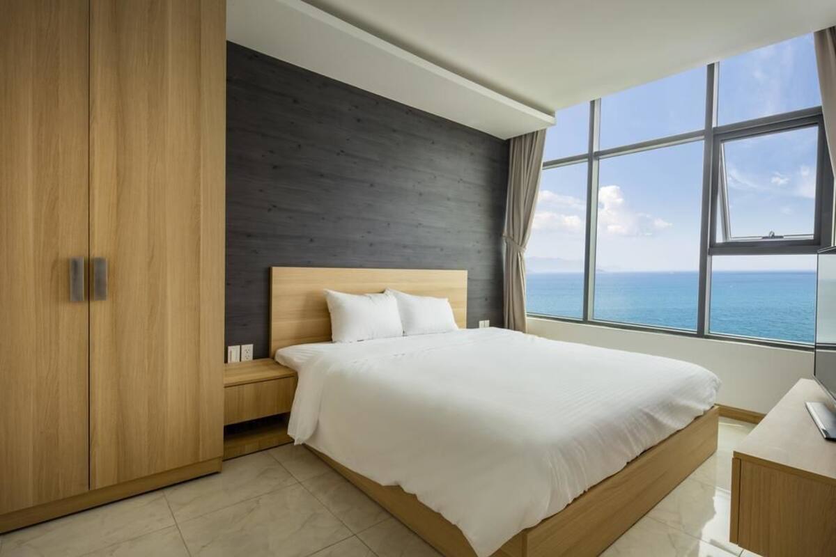A modern bedroom with a large bed, wooden wardrobe, and a view of the sea.