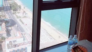 A room with a large window overlooking a beach and cityscape. - Ideal Time Apartment (Nha Trang)