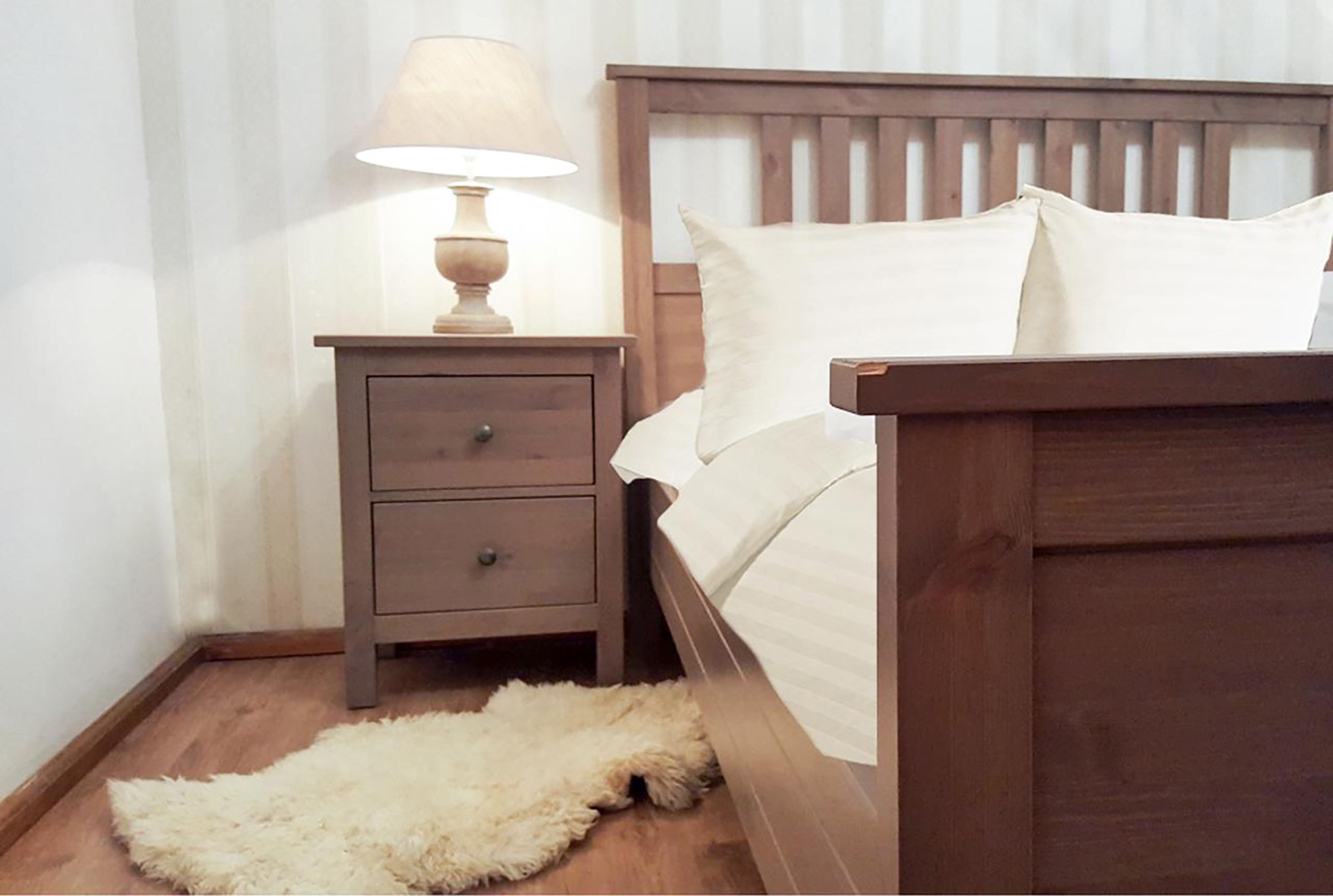 A bedroom with a wooden bed, a nightstand with a lamp, and a fluffy rug on the floor.