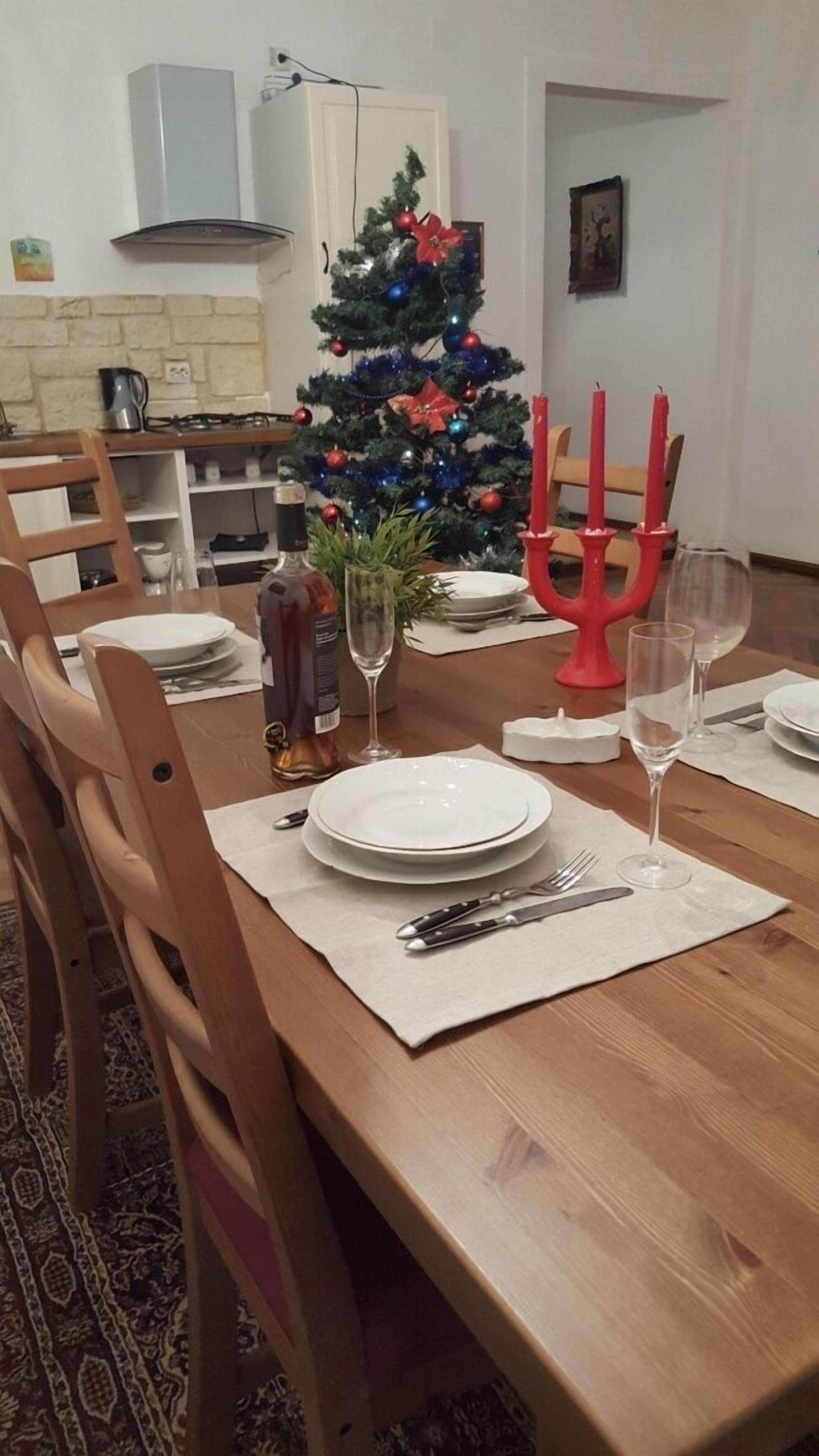 A dining area with a wooden table set for four, a Christmas tree, and red candelabras.