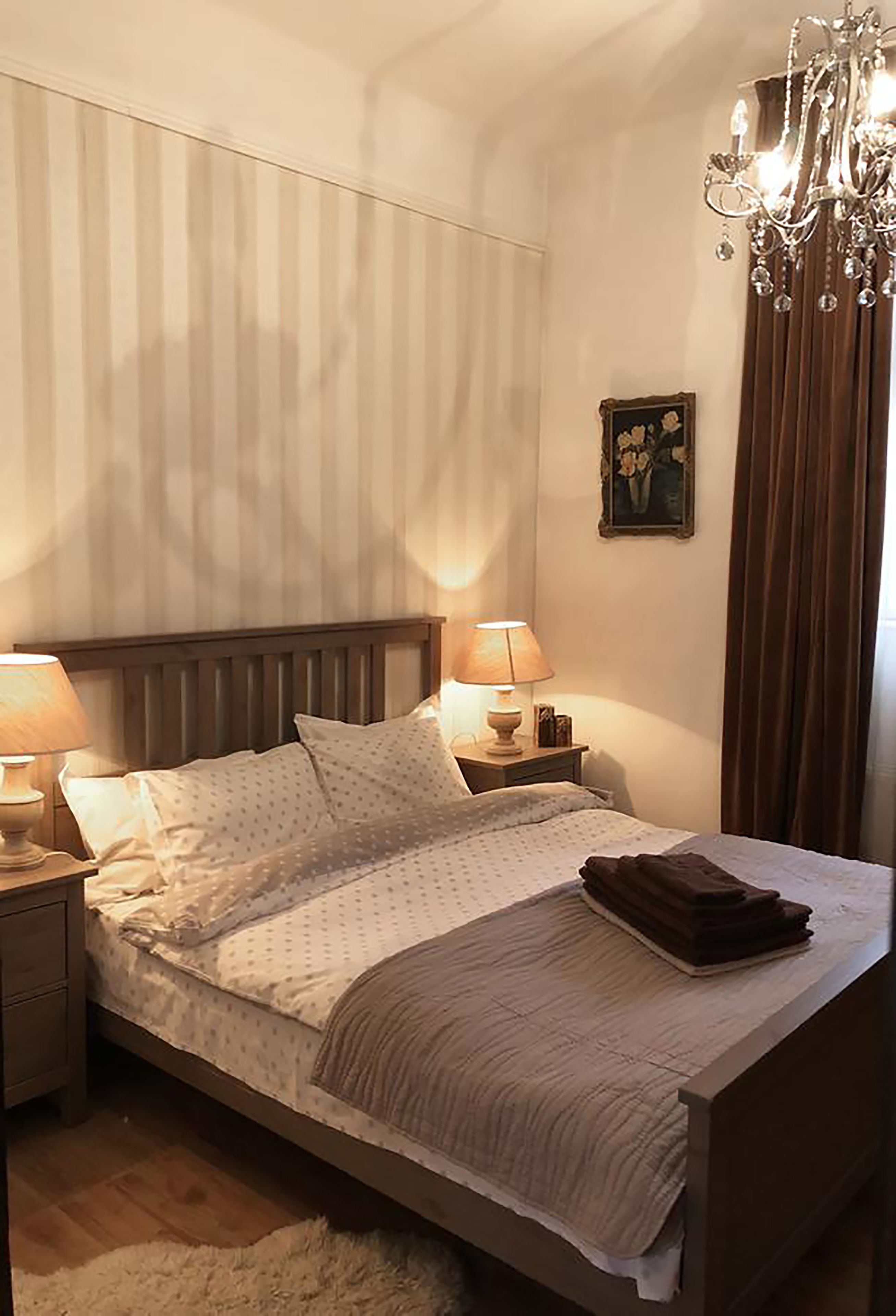 A neatly made bed with a wooden headboard, two bedside lamps, and a chandelier.