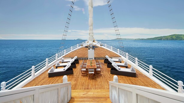 A deck with a wooden floor, white railings, and a central table with chairs. - AYANA Lako di'a (Labuan Bajo)