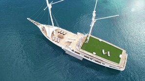 An aerial view of a large yacht with a spacious deck, multiple seating areas, and a green lawn. - AYANA Lako di'a (Labuan Bajo)