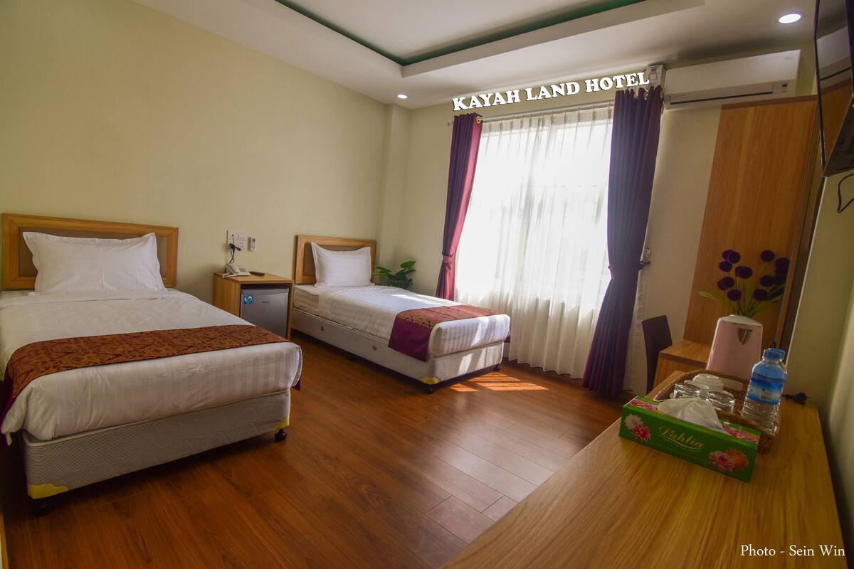 A hotel room with two beds, a desk, a chair, a small table with a bottle, and a box of tissues.