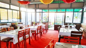 Um restaurante com várias mesas e cadeiras, janelas amplas e um tapete vermelho.