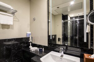 A modern bathroom with a black marble sink, a large mirror, and a glass shower enclosure.