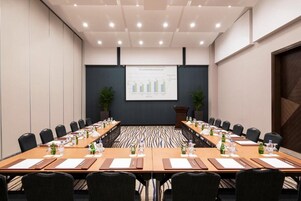Ein Konferenzraum mit einem langen Tisch, Stühlen und einer Präsentationsleinwand.