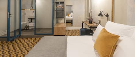 A modern hotel room with a bed, a desk, and a bathroom visible through an open door.