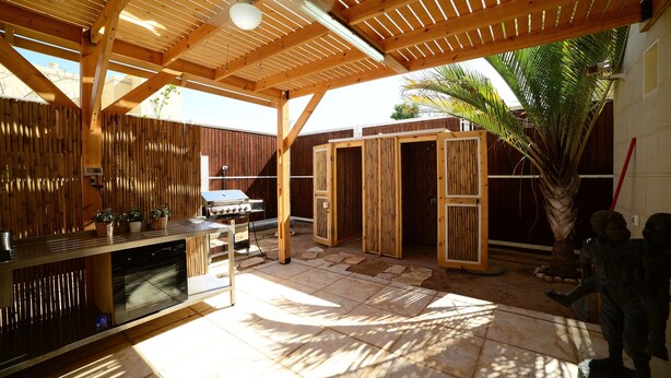 A covered outdoor area with a wooden ceiling, a barbecue grill, and a stone-tiled floor. - Garden Residence (Eilat)