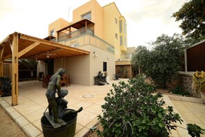 Une cour avec une pergola en bois, une statue représentant un homme et un enfant, et un bâtiment doté d’un balcon.