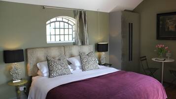 A bedroom with a bed, two bedside lamps, a window with curtains, a small table with a vase, and a chair.