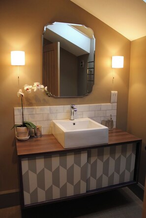 Une salle de bain moderne avec un lavabo blanc, un grand miroir et deux appliques murales.