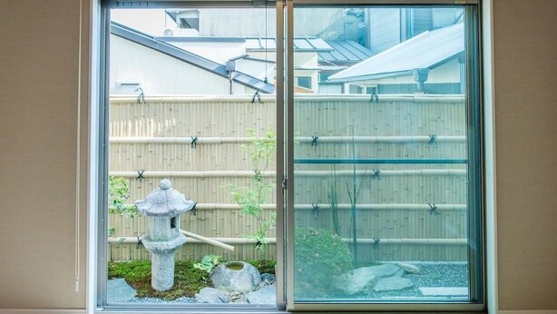 A sliding glass door leading to a traditional Japanese garden with a stone lantern and bamboo fence. - Heartwarming House (Kyoto)