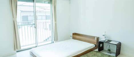 Quarto com cama, mesa de cabeceira, abajur e janela com cortinas.